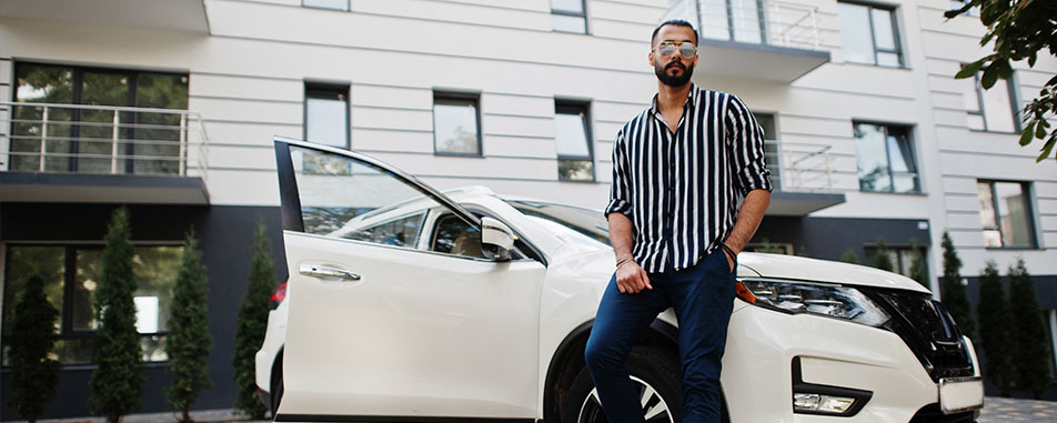 Man in a striped shirt leans on a white car with an open door