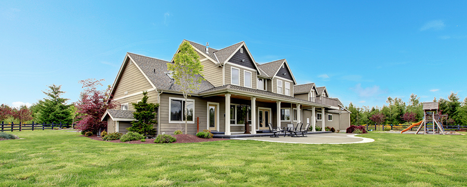 A large, modern house with a gabled roof sits against a bright blue sky