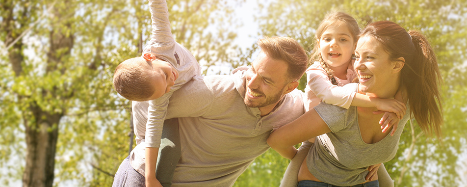 A joyful family of four plays outside, with parents carrying their children on their backs - nyeinsuranceagency.com