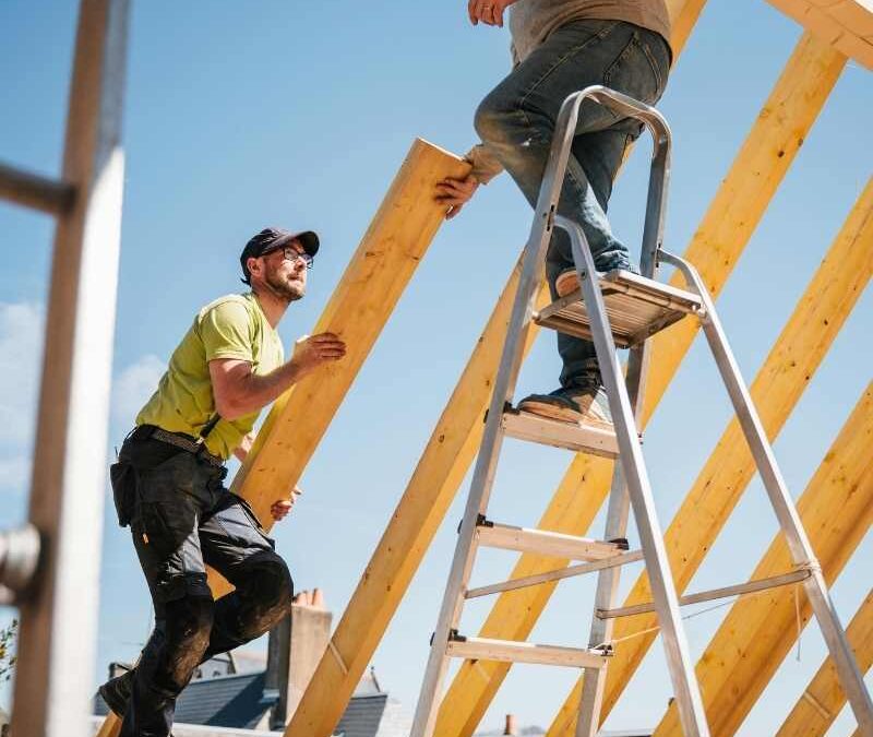 Two construction workers are building a wooden roof frame