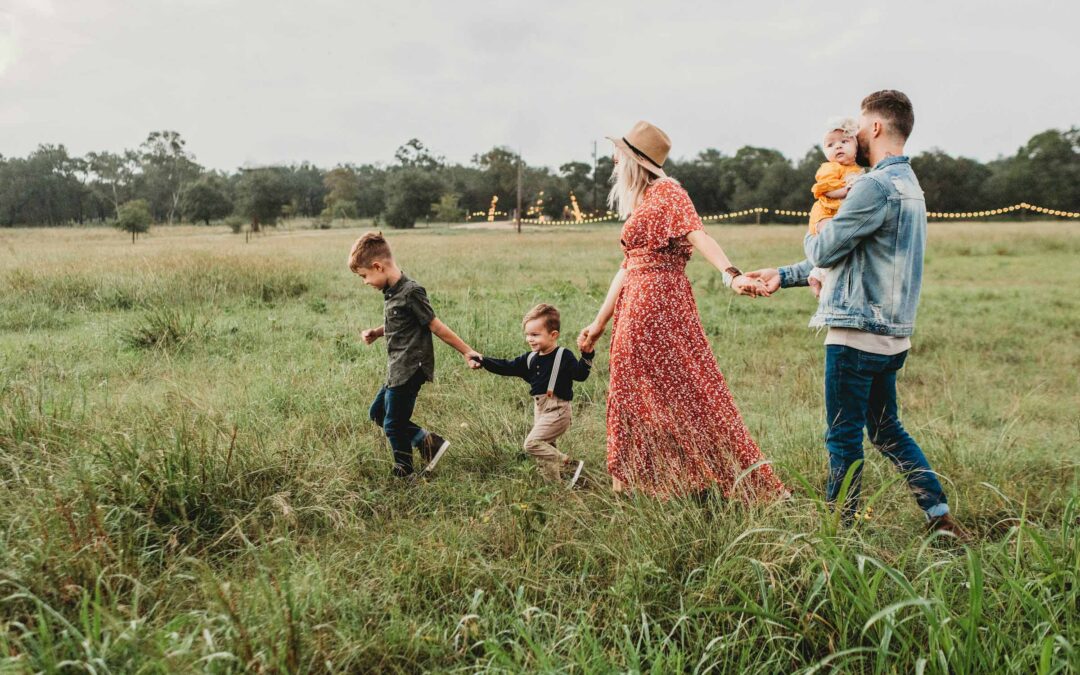 A family joyfully walks together through a lush green field during their outdoor photo session.